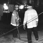 The strain of the long night of the Doxol fire can be seen in this photo of two Grand County Fire Dept. volunteers. Flames can be seen around the propane storage tank in the background, but much reduced in size from the peak of the fire.