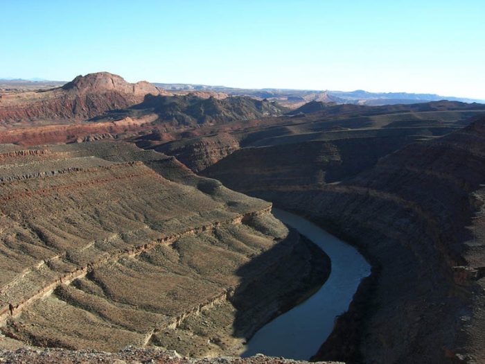 Figure 1. View of the “Mule Ear” (highest point in brown-red sandstone) with dark-gray rubble mass adjacent to it (the Mule Ear diatreme) and the entrance into the upper canyon of the San Juan River as it cuts across the east-dipping strata of the Monument upwarp. View from Lime Ridge. (G.M. Stevenson photo)